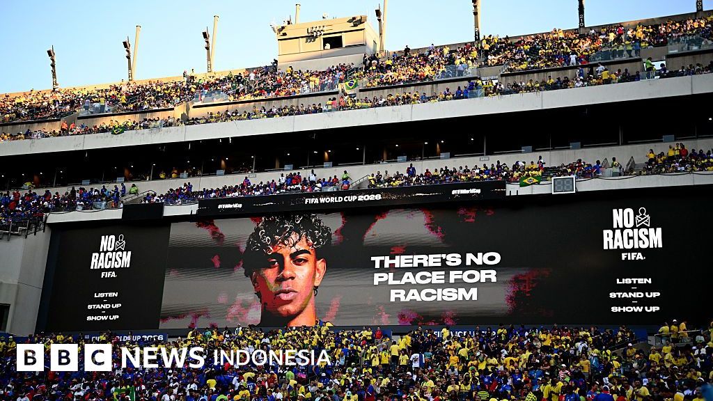 Seorang pemain sepak bola menunjukkan gestur anti-rasisme di tengah pertandingan. Perjuangan melawan kebencian di lapangan dan dunia maya terus berlanjut.