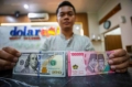 Petugas menunjukkan pecahan dolar AS dan rupiah di gerai penukaran mata uang asing, merefleksikan volatilitas nilai tukar yang terjadi.